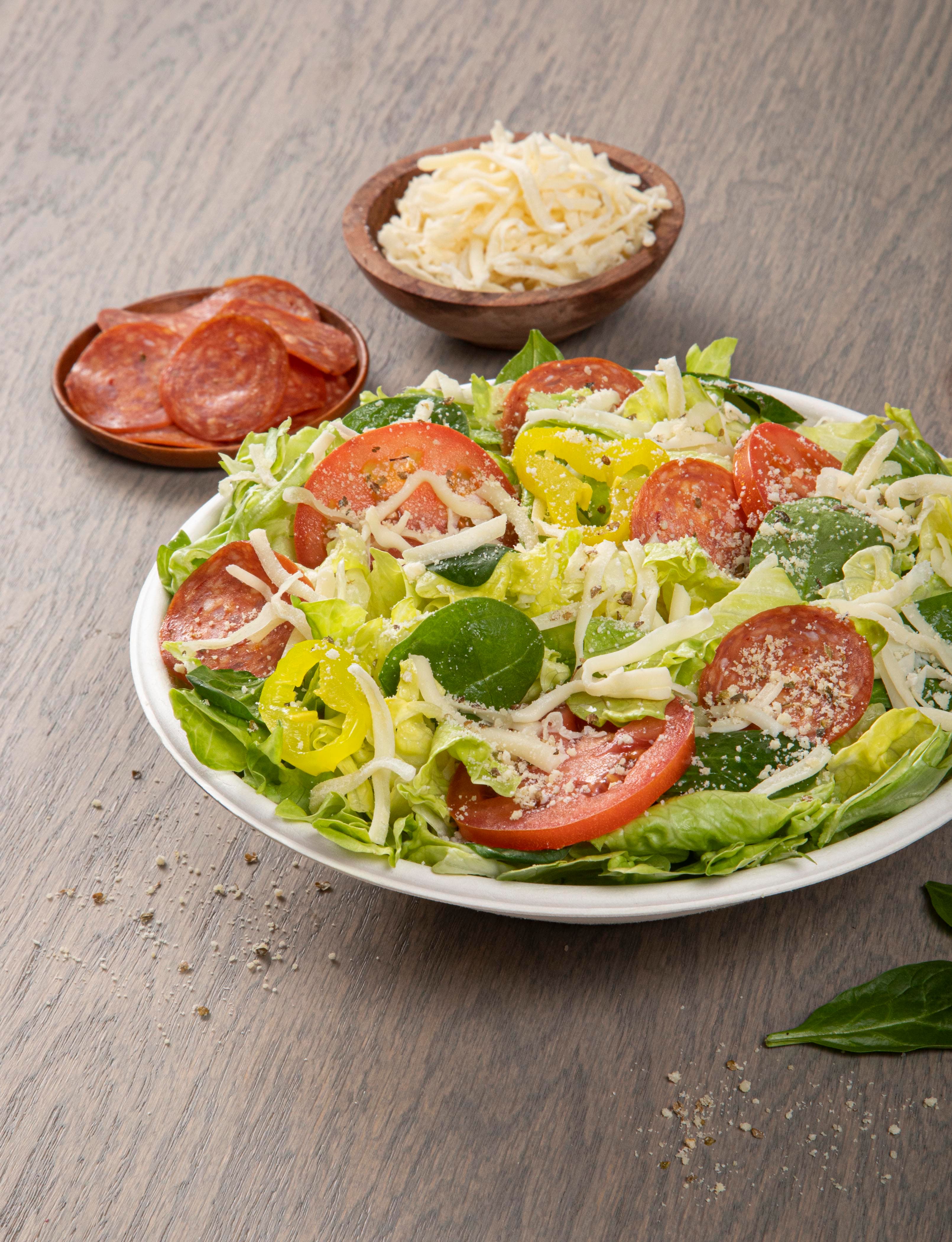A Donatos Italian Side Salad in a white bowl with tomato, pepperoni, banana peppers and shredded cheese
